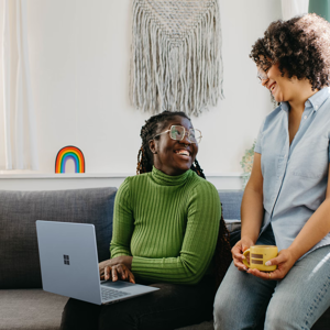 2 vrouwen zitten op een bank met een laptop en een kop koffie